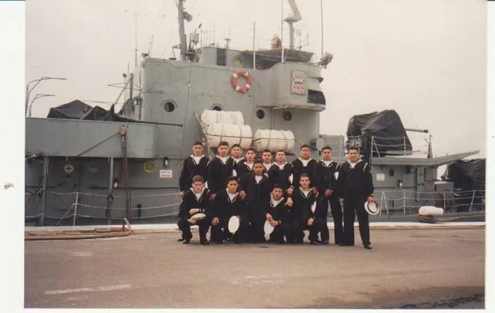 Gustavo and fellow sailors assembled in front of a Navy ship.